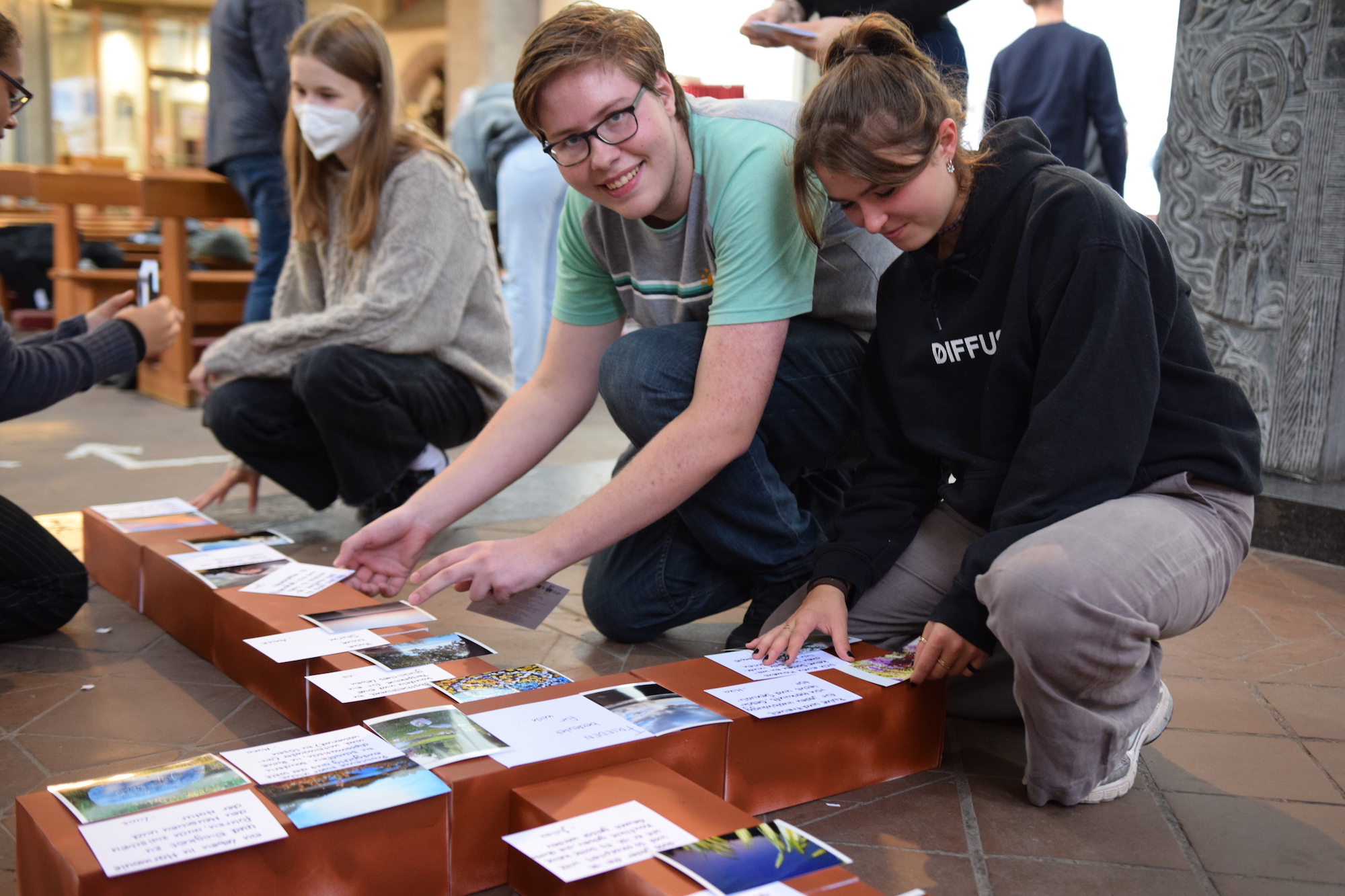 Schülerinnen und Schüler des Inda-Gymnasiums heften ihre Gedanken zum Frieden an ein Kreuz, das sie aus besprühten Schuhkartons zusammengelegt haben.